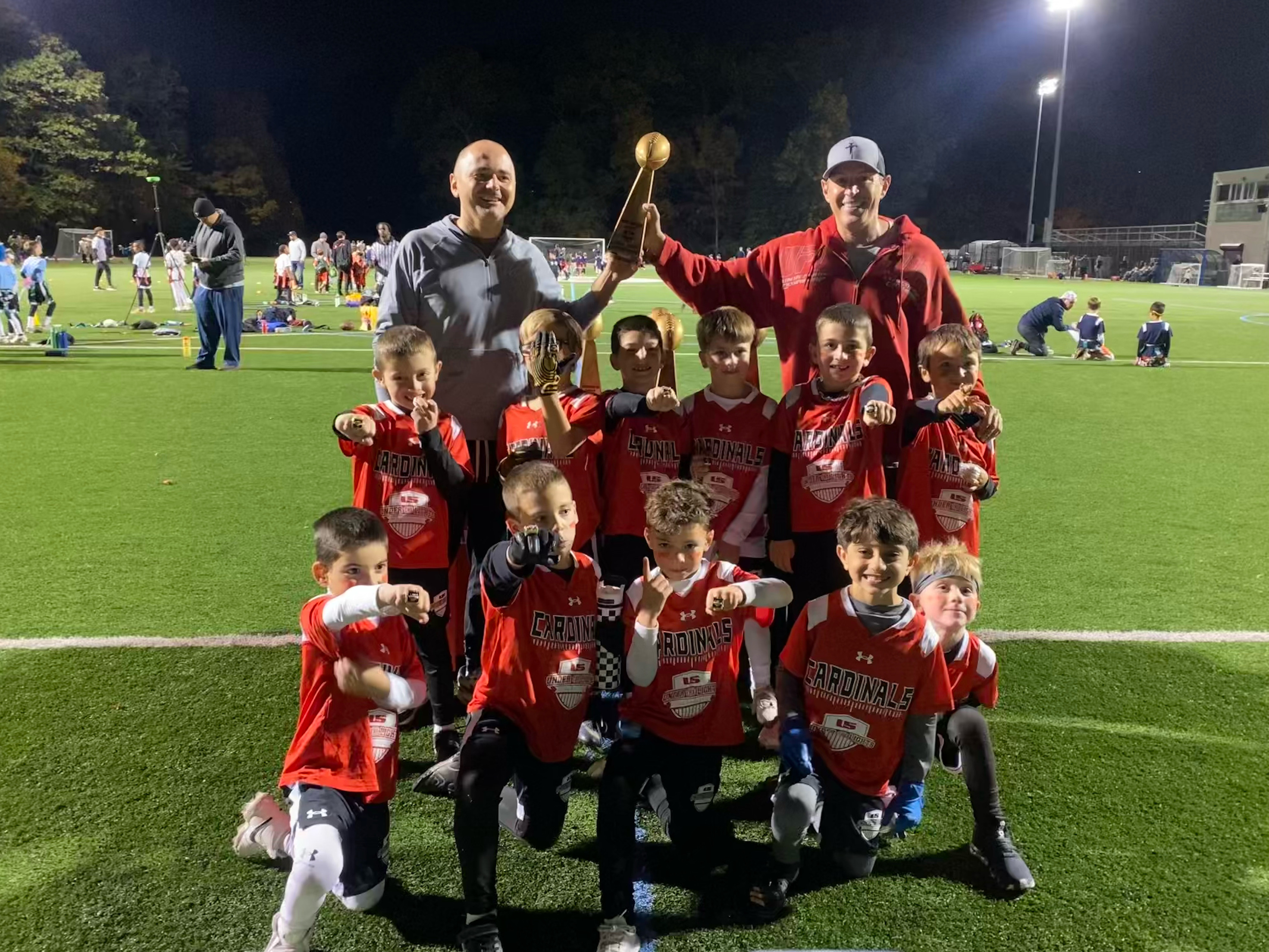 Cardinals youth flag football champions celebrating with Biagio Maffettone and trophy.